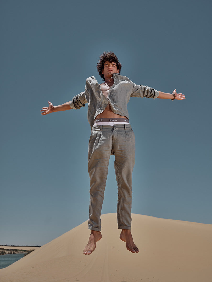 Person jumping on a sand dune with a clear blue sky wearing linen shirt and pants