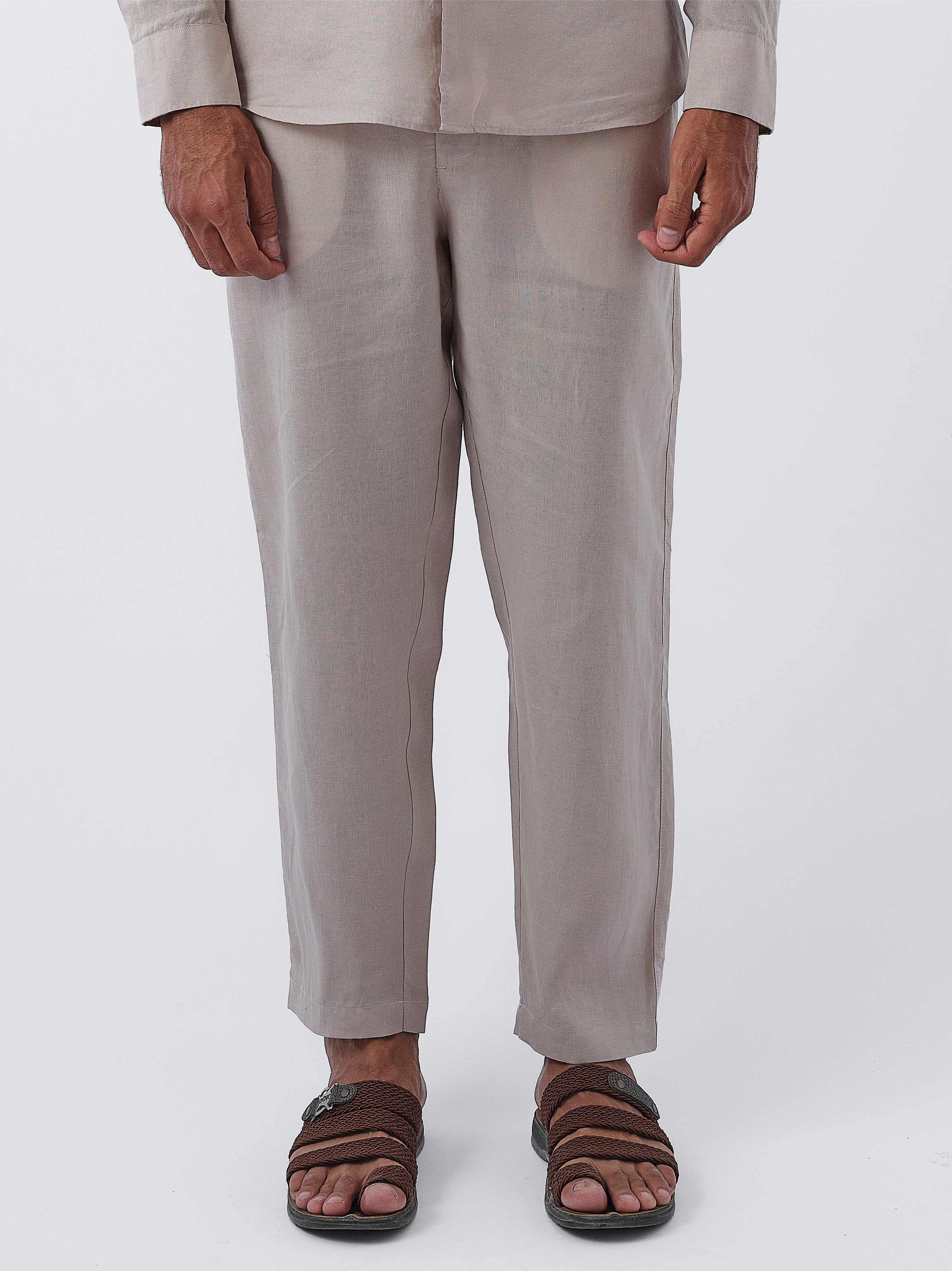 Person wearing beige pants and brown sandals on a white background