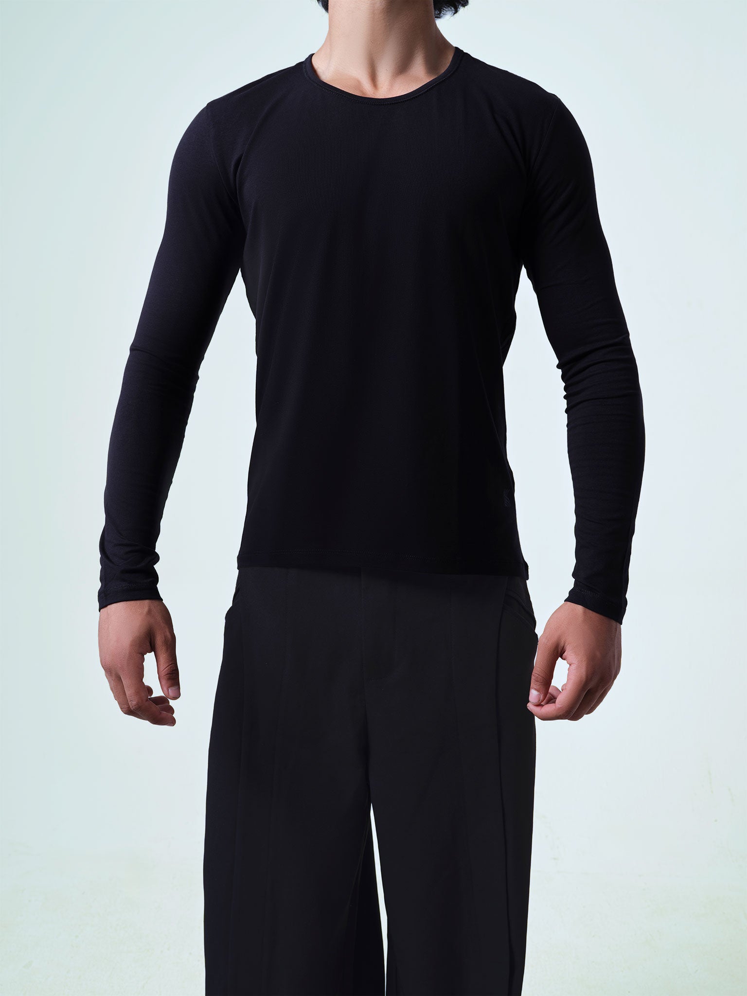 Person wearing a black long-sleeve crew-neck shirt and black pants against a light gray background