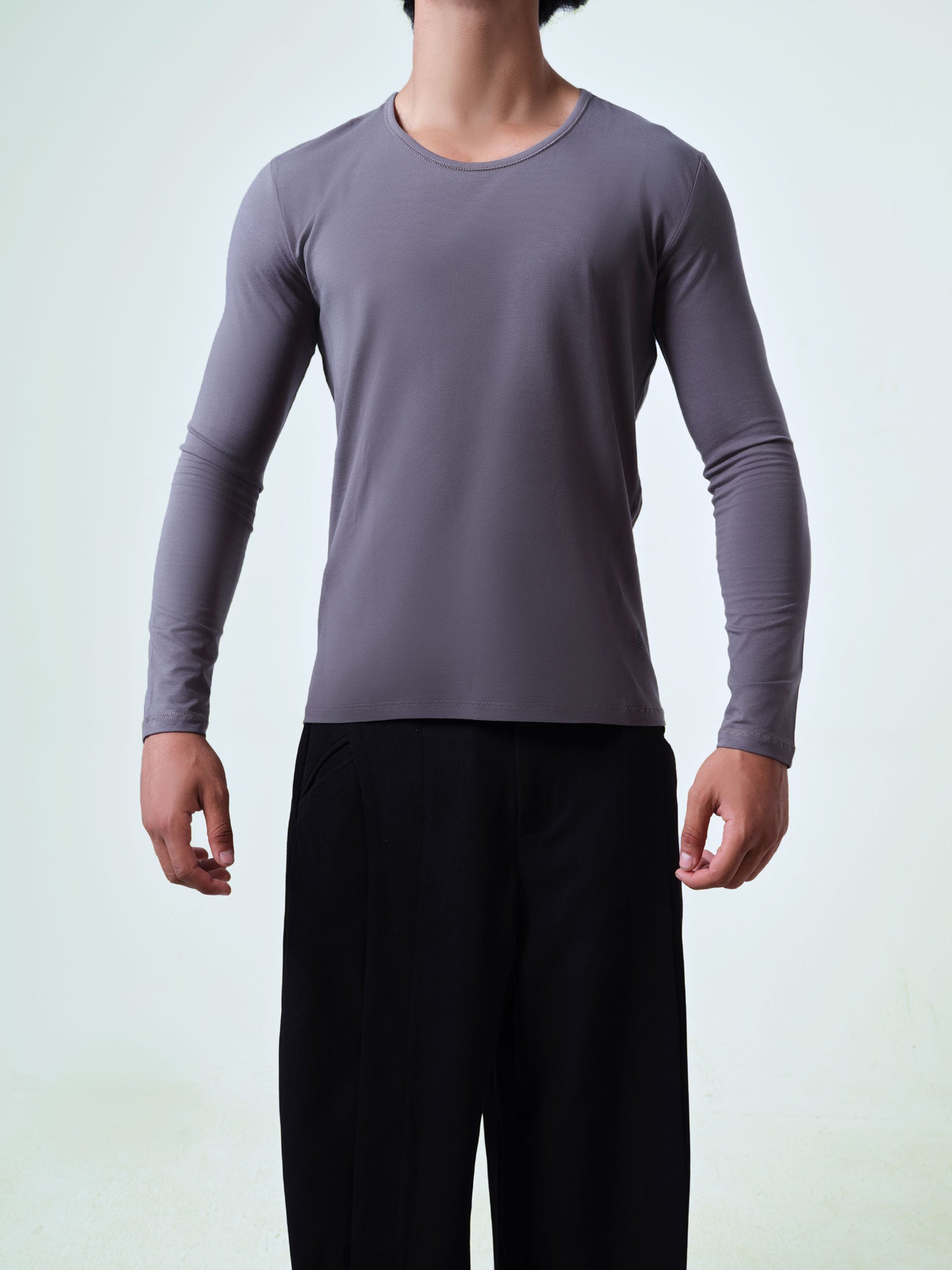 Person wearing a gray long-sleeve crew neck shirt and black pants on a light gray background.